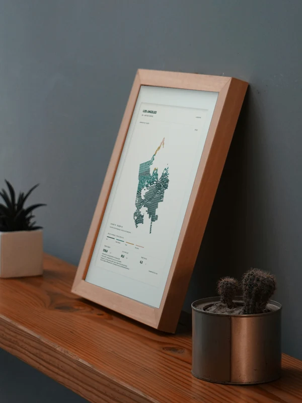 The Los Angeles artwork digitally placed in a frame on a shelf beside plants. Framing and proportions are illustrative.